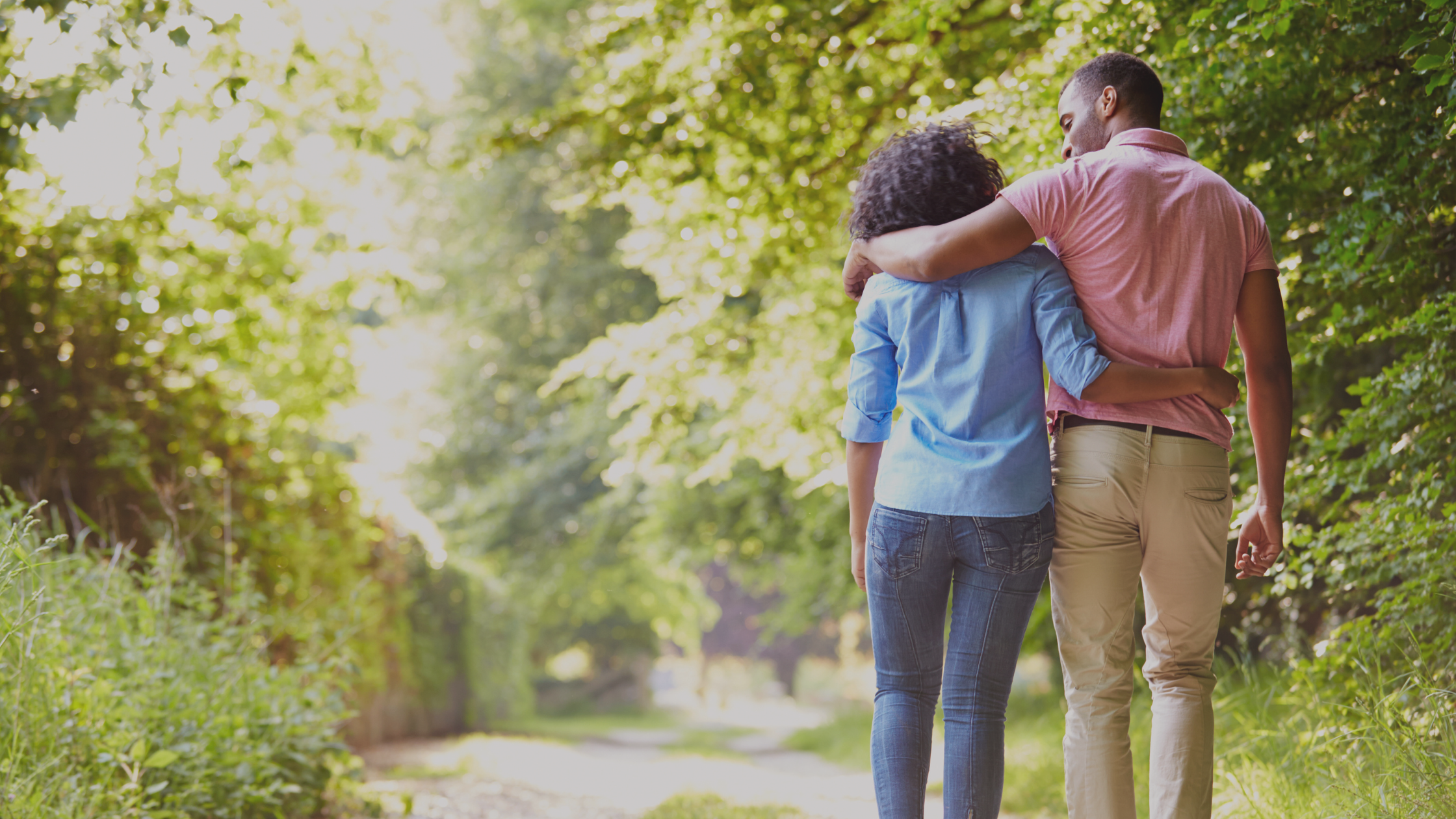 Man and woman walking with arms around each other on a path outdoors.